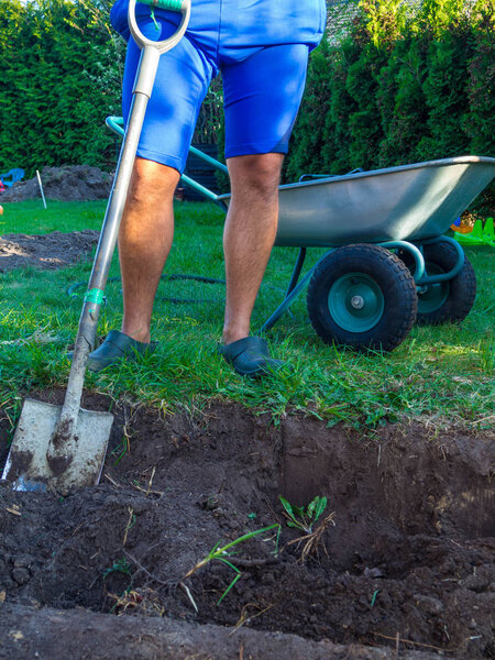man digging a garden for new plants, and wheelbarrow in garden