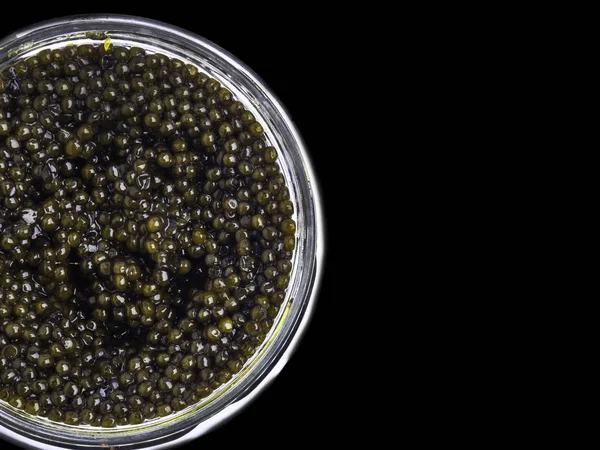 Caviar preto em uma tigela pequena em um fundo preto, vista superior — Fotografia de Stock