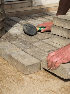 Bricklayer bir veranda çekiç aracı oluşturmak için beton kaldırım taş bloklar yerleştirir