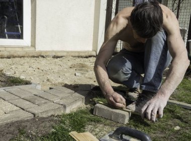 Bricklayer çekiç kullanarak, bir veranda oluşturmak için beton kaldırım taş bloklar yerleştirir