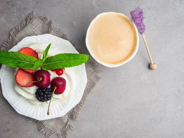 Delicioso pastel Pavlova con capas alternas de crema batida y merengue cubierto con bayas frescas, y taza de café con café con leche fresca — Foto de Stock