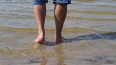 Deniz kıyısında yürüyen adam. Su üzerinde yürüyüş. Vahşi doğa. Adam deniz 4k, kot şort erkekler bacaklar gider