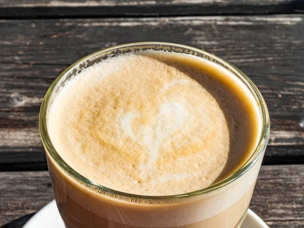 Copo de vidro de café latte com forma de coração bonito, mesa de madeira — Fotografia de Stock