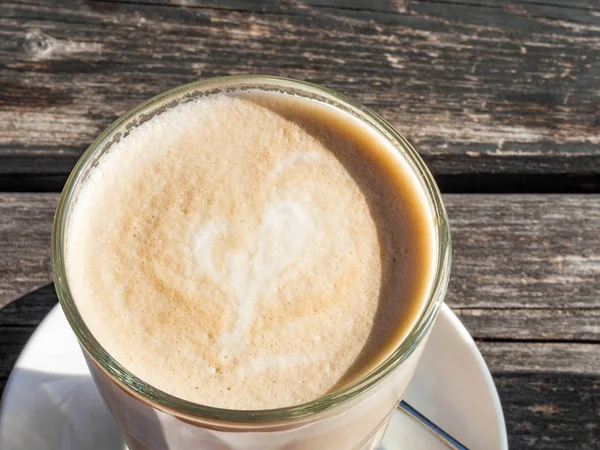 Copa de vidrio de café con leche con forma de corazón hermoso, mesa de madera — Foto de Stock