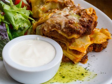 Baharatlı domates bazlı kıyma ve eritilmiş mozzarella peyniri ile geleneksel İtalyan lazanya lezzetli hizmet erişte katmanları arasında, krema ve yeşil yapraklı