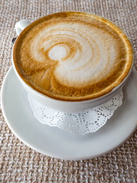 Capuchino caliente con espuma y patrón sobre fondo de paño, una vista lateral — Foto de Stock