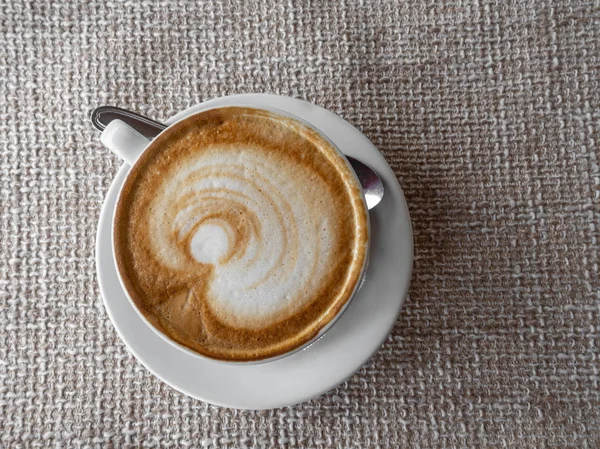 Kopi cappuccino atau latte dalam cangkir elegan putih dengan piring, pada kain karung pedesaan latar belakang. Minuman panas pagi. Gaya hidup kopi . — Stok Foto