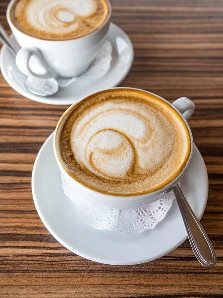 Dwie filiżanki cappuccino z Latte Art na drewnianym tle. Gorąca kawa na stole. Widok z boku. Piękna pianka — Zdjęcie stockowe