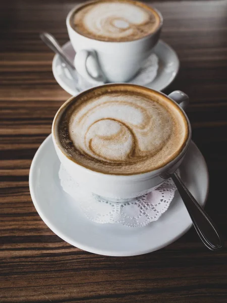 Zwei Tassen Cappuccino mit Latte Art auf Holzgrund. heißer Kaffee auf dem Tisch. Seitenansicht. schöner Schaum — Stockfoto