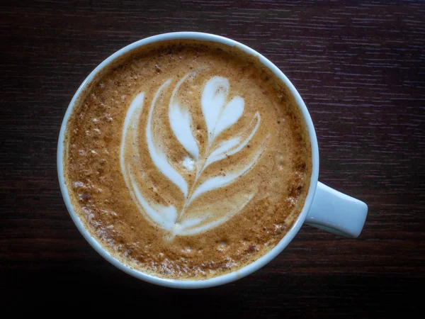 Café caliente en una taza con leche espuma hermoso arte latte sobre fondo de mesa de madera. Cappuccino o latte con espuma espuma — Foto de Stock