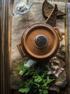 Bir kil tencerede Rus çorbası, ekmek yanında, ekşi krema, yeşillik, ahşap yüzeyde domuz yağı