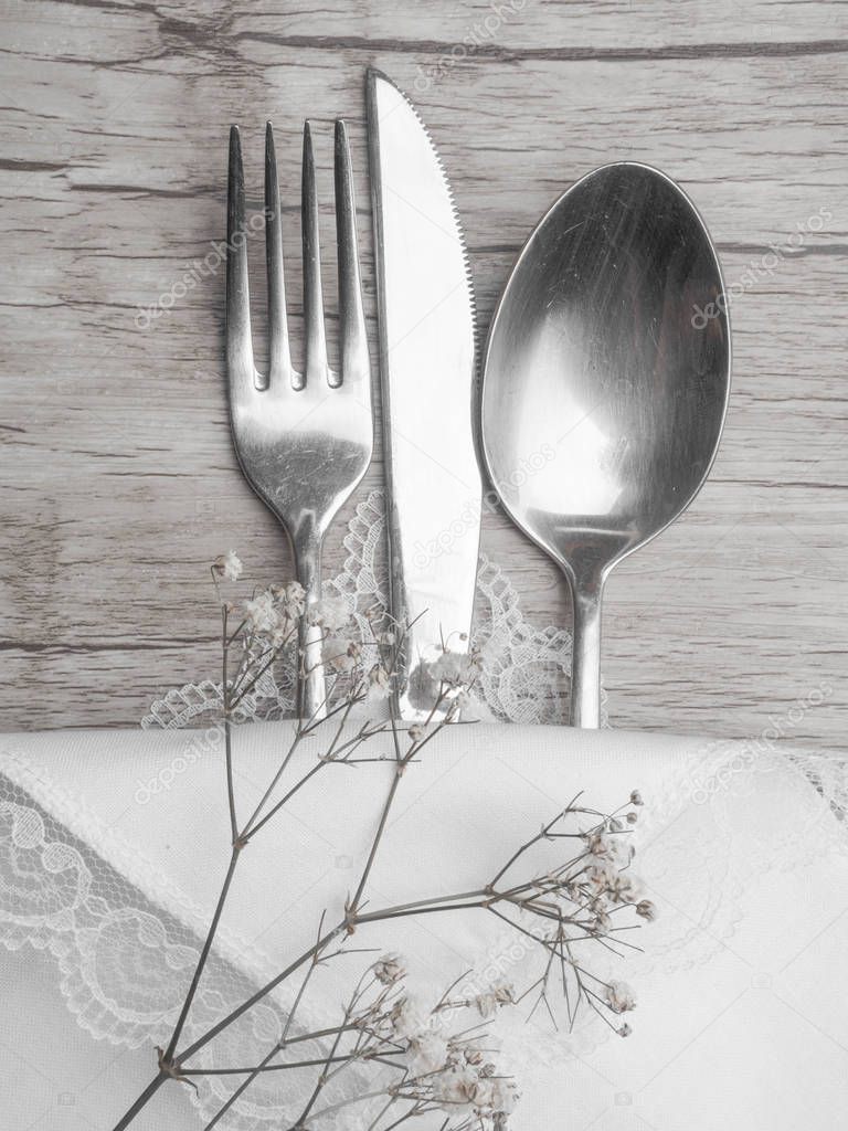 Festive Greeting Card Merry Christmas and Happy New Year, Winter holiday dinner spoon, fork, knife on white napkin on wood background, with white flowers decoration