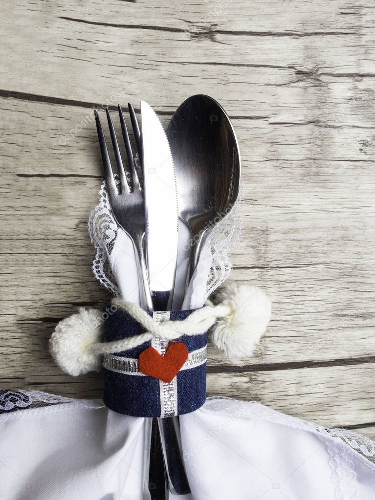 Festive Greeting Card Winter holiday dinner spoon, fork, knife on white napkin decorated with heart shape, soft pompoms on white wood background