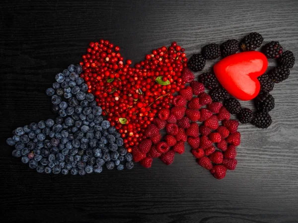 Heart of berries on a wooden background. Red raspberries, cranberry, blueberry, blackberry. Tasty, vitamin food.