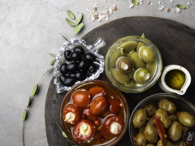 İtalyan gıda maddeleri Cam kase ve zeytinyağı siyah ve yeşil zeytin, peynir küçük biber ve kırmızı kızılcık, otlar ile doldurulmuş. Metin için alan ile beton arka plan üzerinde üst görünüm.