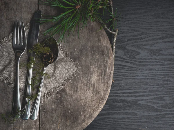 Dekor olarak havlu, çuval bezi ve yeşil dalı ile Noel masa ayarı, ahşap tahta üzerinde gümüş. Üstte görüntü.