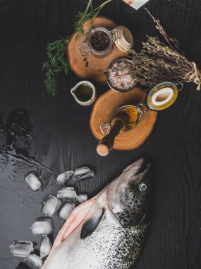 Buz küpleri somon balık, siyah ahşap masa üzerinde pişirme için malzemelerle çiğ somon balık bütün. Üst te. Tonda