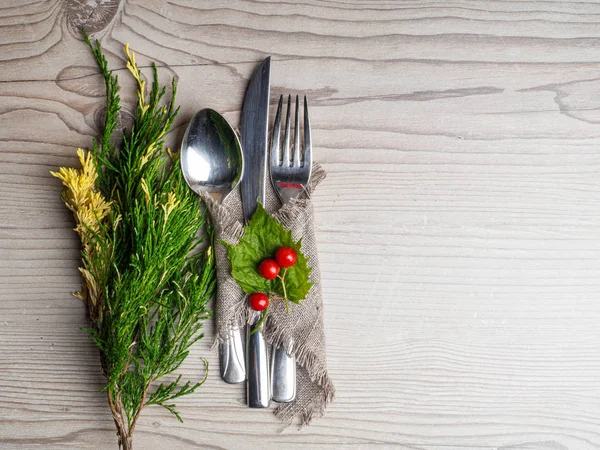 Christmas table: knife spoon fork, burlap napkin and Christmas tree branch on a wooden table top view with copy space. New Year\'s decor of the festive table.
