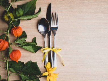 bir bıçak, kaşık ve çatal ile sonbahar temalı yer ayarı, sarı çiçek, physalis dalı ile süslenmiş