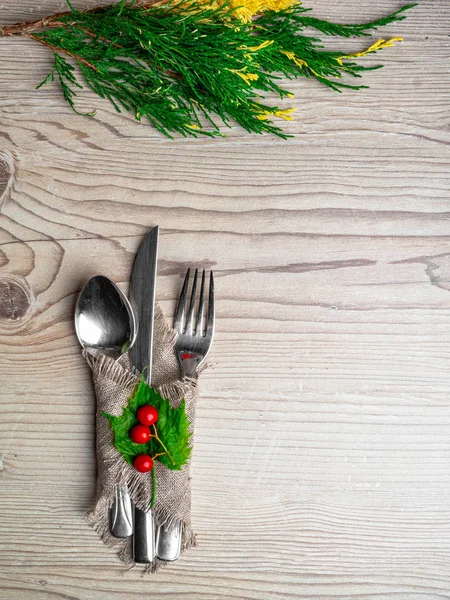 Christmas table: knife spoon fork, burlap napkin and Christmas tree branch on a wooden table top view with copy space. New Year\'s decor of the festive table.