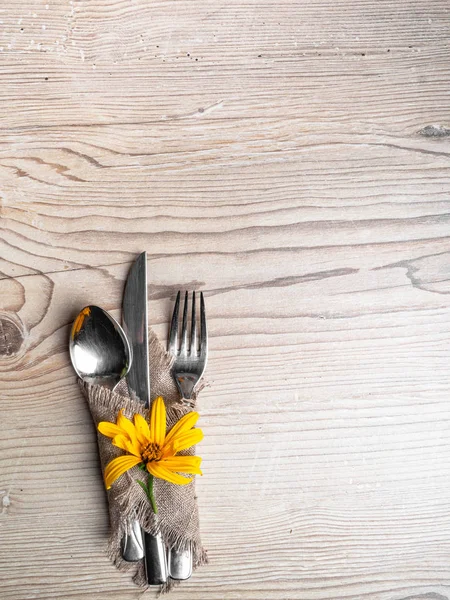 Rustic table setting with linen napkin, cutlery, yellow lower on wooden table. Holiday table decoration. Romantic dinner.