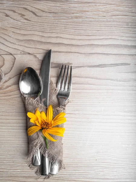 Rustic table setting with linen napkin, cutlery, yellow lower on wooden table. Holiday table decoration. Romantic dinner.