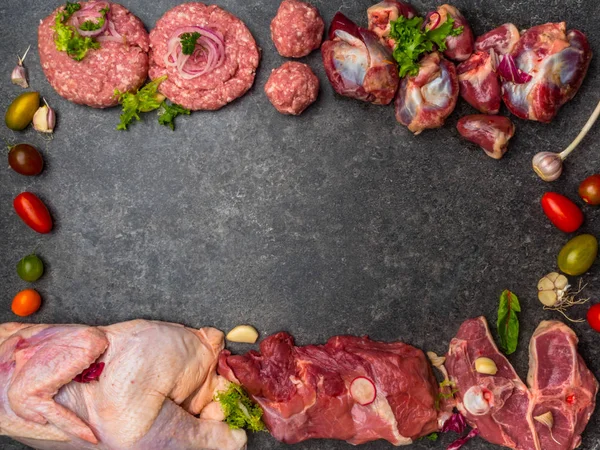 Carne cruda surtida sobre fondo oscuro, con tomates cherry, ajo, cebolla y verduras, espacio para copiar — Foto de Stock