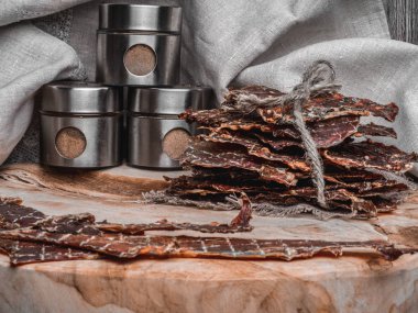 Kavanozlarda baharatlarla kurutulmuş veya kurutulmuş et dilimleri, ahşap arka plan, kopyalama alanı