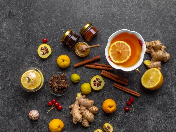 Hot drink with honey, lemon and ginger for cough remedy on concrete background, with propolis in glass bowl, cydonia, cinnamon sticks, red berries