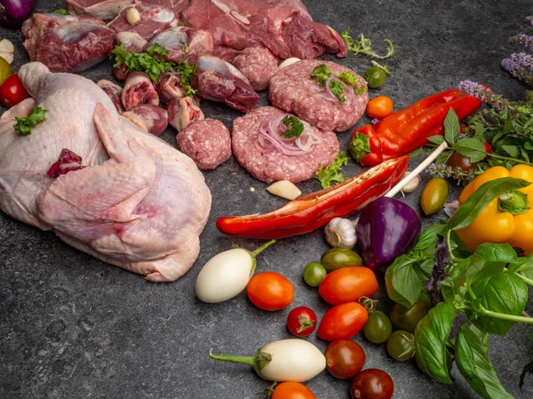 Different types of raw meat: beef, chicken, lamb, gilbert, pork, herbs, lettuce, garlic, cherry tomatoes, bell pepper, greenery