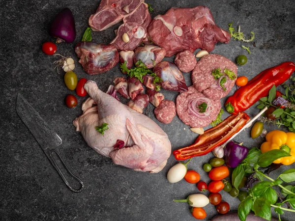 Different types of raw meat: beef, chicken, lamb, gilbert, pork, herbs, lettuce, garlic, cherry tomatoes, bell pepper, greenery