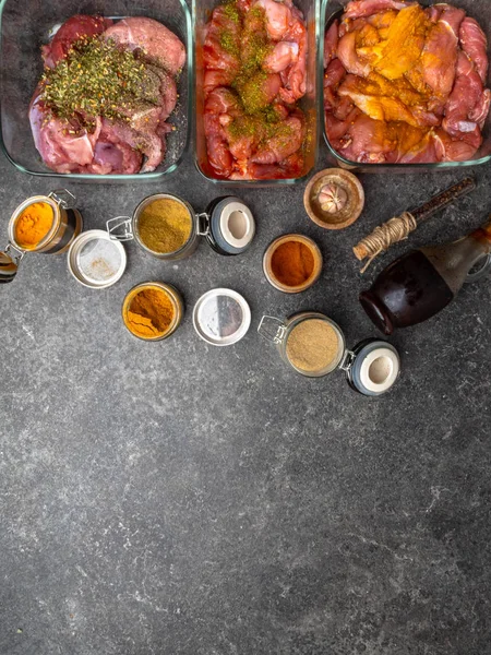 Verschiedene eingelegtes Fleisch in Glasschalen und Gläser mit Gewürzen und Kräutern wie Kurkuma, Kardamon, Rosmarin, schwarzem Pfeffer, Soja- und Granatapfelsoße auf grauem Hintergrund — Stockfoto