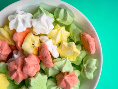 Pastel naneli arkaplanda renkli merengelerle dolu seramik vazo