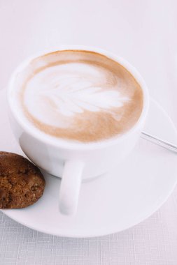 Beyaz sanat latte ya da tek çikolatalı kurabiye ile kapuçino kahve fincanı.