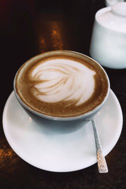 Bir fincan sıcak latte ya da kapuçino sanat kahvesi beyaz bardakta, köpüklü, aydınlatma arka planlı kafede.