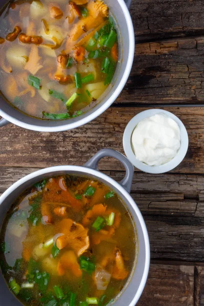 Bowl of soup with autumn chanterelles and herbs, green onion, bread slices, sour cream on rusrtic wooden background. Vegetarian Russian cuisine, Top view — Stock Image Bowl Soup Autumn Chanterelles Herbs Green Onion Bread Slices Sour Stock Photo