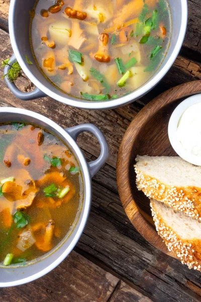 Bowl of soup with autumn chanterelles and herbs, green onion, bread slices, sour cream on rusrtic wooden background. Vegetarian Russian cuisine, Top view — Stock Image Bowl Soup Autumn Chanterelles Herbs Green Onion Bread Slices Sour Stock Image