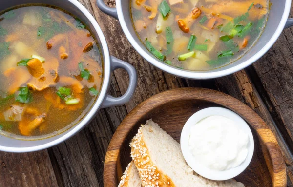 Bowl of soup with autumn chanterelles and herbs, green onion, bread slices, sour cream on rusrtic wooden background. Vegetarian Russian cuisine, Top view — Stock Image Bowl Soup Autumn Chanterelles Herbs Green Onion Bread Slices Sour Stock Picture