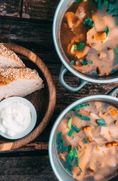 Bowl of soup with autumn chanterelles and herbs, green onion, bread slices, sour cream on rusrtic wooden background. Vegetarian Russian cuisine, Top view — Stock Image Bowl Soup Autumn Chanterelles Herbs Green Onion Bread Slices Sour Royalty Free Stock Photos