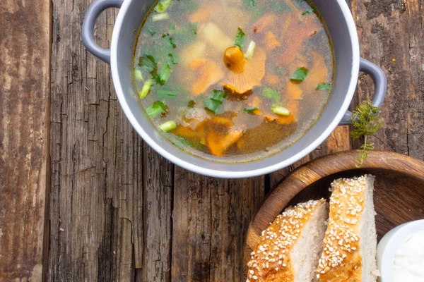 Bowl of soup with autumn chanterelles and herbs, green onion, bread slices, sour cream on rusrtic wooden background. Vegetarian Russian cuisine, Top view — Stock Image Bowl Soup Autumn Chanterelles Herbs Green Onion Bread Slices Sour Stock Image