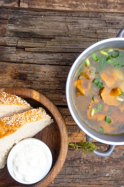 Bowl of soup with autumn chanterelles and herbs, green onion, bread slices, sour cream on rusrtic wooden background. Vegetarian Russian cuisine, Top view — Stock Image Bowl Soup Autumn Chanterelles Herbs Green Onion Bread Slices Sour Stock Photo