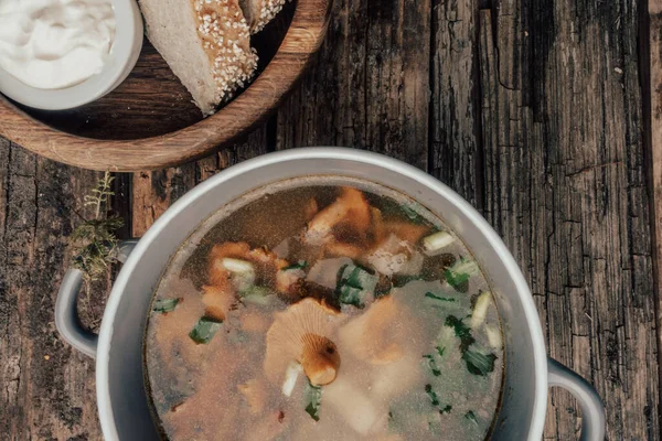 Bowl of soup with autumn chanterelles and herbs, green onion, bread slices, sour cream on rusrtic wooden background. Vegetarian Russian cuisine, Top view — Stock Image Bowl Soup Autumn Chanterelles Herbs Green Onion Bread Slices Sour Stock Picture