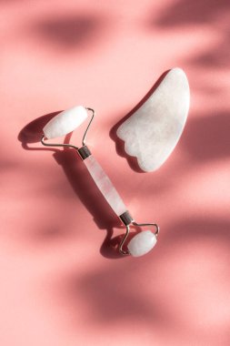 Yüz bakımı ve yüz masajı için pembe doğal kuvars silindiri, güneşli ve modaya uygun zıt gölgeler. Gua Sha aletleri. Yaş karşıtı, evde rahatlama kaldırma ve alternatif tıp kavramı