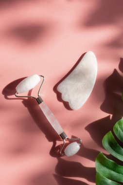 Yüz bakımı ve yüz masajı için pembe doğal kuvars silindiri, güneşli ve modaya uygun zıt gölgeler. Gua Sha aletleri. Yaş karşıtı, evde rahatlama kaldırma ve alternatif tıp kavramı