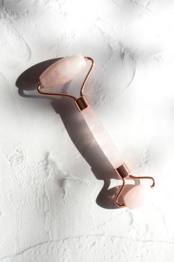 Beton beyaz arka planda kuvars taşı silindiri, masaj aleti. Evde yüz bakımı, yaşlanma önleyici rahatlama, detoks ve kaldırma terapisi. Kapat.