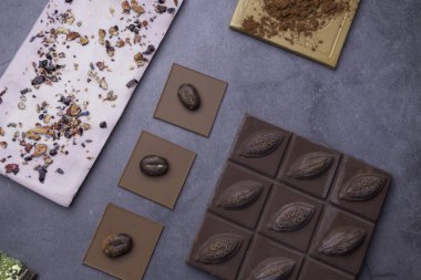 Koyu, süt, fındık ve beyaz çikolatadan yapılmış çikolata parçalarının karışımı. Fasulyeli, kakaolu, gri betondan sırtüstü uzanan. Seçici odak