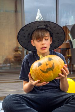 Cadılar Bayramı kostümlü çocuk, şapka ve sonbahar balkabakları ahşap terasta, cadılar bayramı, bayram ve çocukluk konsepti