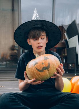 Cadılar Bayramı kostümlü çocuk, şapka ve sonbahar balkabakları ahşap terasta, cadılar bayramı, bayram ve çocukluk konsepti