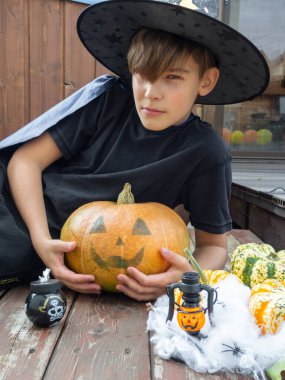 Cadılar Bayramı kostümlü çocuk, şapka ve sonbahar balkabakları ahşap terasta, cadılar bayramı, bayram ve çocukluk konsepti