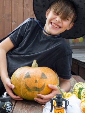 Cadılar Bayramı kostümlü çocuk, şapka ve sonbahar balkabakları ahşap terasta, cadılar bayramı, bayram ve çocukluk konsepti